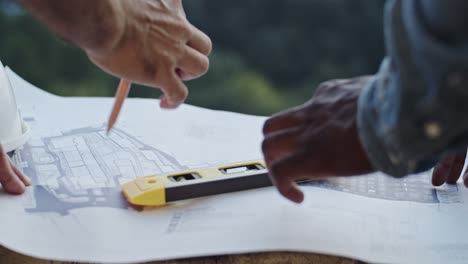 Close-up-of-the-Caucasian-and-African-American-male-hands-pointing-something-on-the-drafts-and-plans-while-men-builders-and-architects-working-over-the-project.